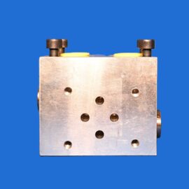 Close-up of a metal hydraulic/manifold block with yellow seals and dark studs, set against a solid blue background.