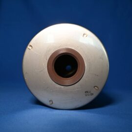 Close-up of a scratched metal circular plate with a central bore and brown inner ring, set against a blue background.