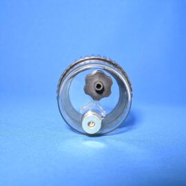 Close-up of a circular metal device with a serrated gear edge and clear glass lens against a blue background.