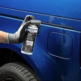 Gloved hand holding a spray can applying touch-up paint to the side of a blue van.
