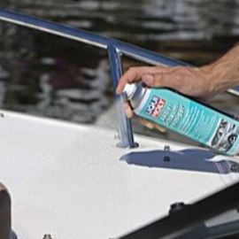 Person spraying a cleaning product onto the deck of a white boat near the blue railing.