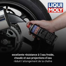 Person applying Liqui Moly chain lubricant to a motorcycle chain; logo visible in corner, French caption about water resistance and reducing chain wear.