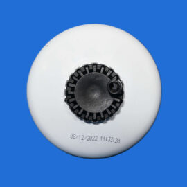 Close-up of a white circular device with a black serrated adjustment knob, on a blue background, with a date/time imprint visible.