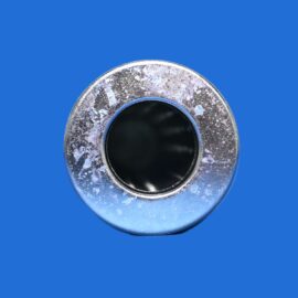 Close-up of a silver metallic ring with a dark inner hole on a solid blue background, showing a weathered finish.