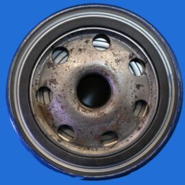 Close-up of a rusty metal pulley wheel with circular holes, against a bright blue background.